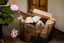 Load image into Gallery viewer, Wire log basket of hardwood logs outside a door next to some flowers.
